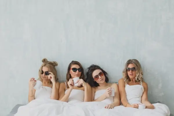 ארבע נשים עם שמלות לבנות יושבות ונשענות על קיר אפור