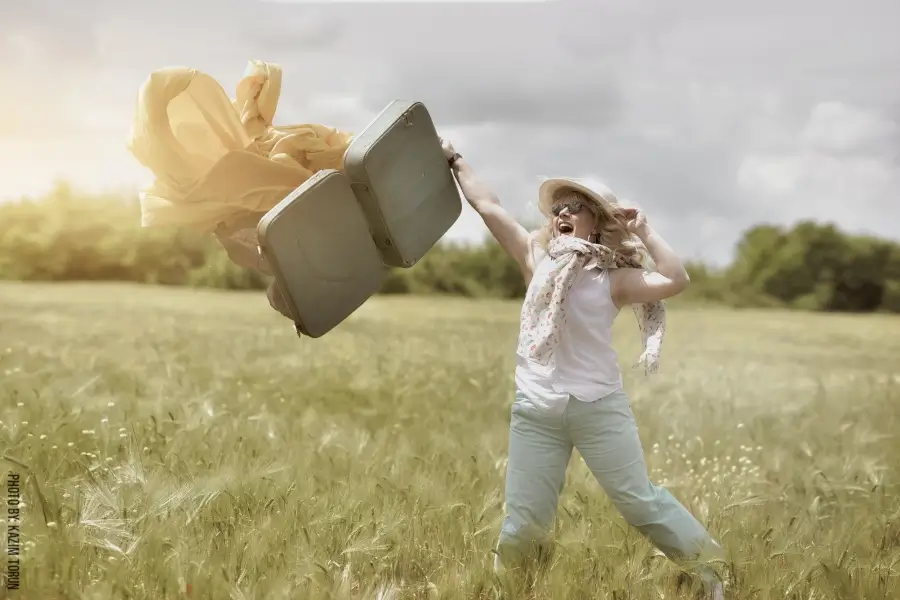 אישה שמחה זורקת מזוודה באוויר על רקע שדה פתוח